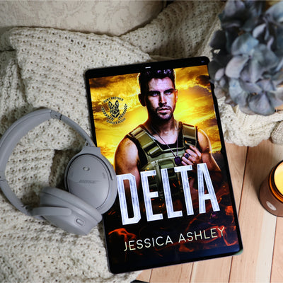 A tablet displaying a book cover titled 'DELTA' by Jessica Ashley, styled on a cream knit blanket with gray Bose headphones and dried flowers nearby.