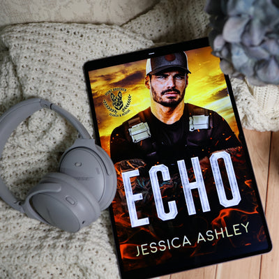 A tablet displaying a book cover titled 'ECHO' by Jessica Ashley, styled on a cream knit blanket with gray headphones and a decorative flower nearby.