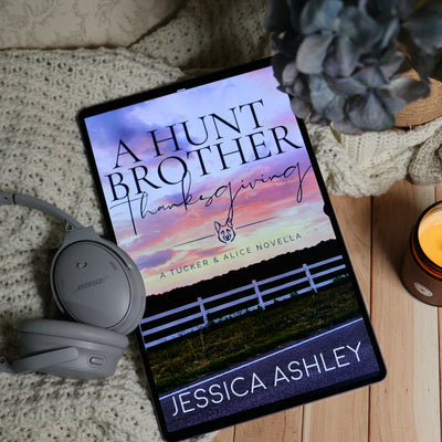 A tablet lying on a knitted blanket with a candle, headphones, and flowers around it, displaying the book cover for 'A Hunt Brother Thanksgiving' by Jessica Ashley.