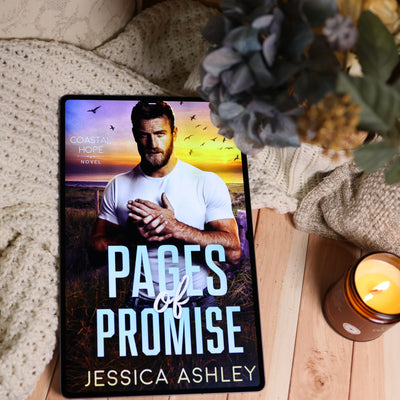 A tablet displaying the book cover of 'Pages of Promise' by Jessica Ashley, styled on a wooden surface with a cozy knit blanket, a lit candle, and dried flowers.