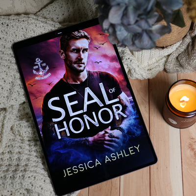 A tablet or book cover displaying the title 'SEAL OF HONOR' by Jessica Ashley, styled on a wooden surface with a knitted blanket, a lit candle, and dried flowers.
