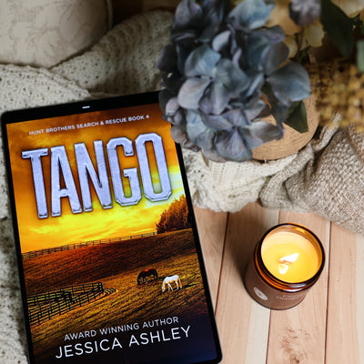 A tablet displaying the book cover of 'Tango' by Jessica Ashley, styled on a wooden surface with a lit candle, knitted blanket, and blue hydrangeas.